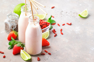 Healthy blended superfood drink. Organic diet smoothie with strawberry and goji berries, chia seeds and lime. Glass bottles with eco fendley straws. Gray background with copy space