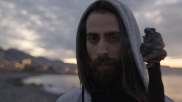 Young hipster bearded long-haired hoodie man is holding a burning torch in his hand by the sea.