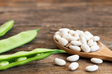 Uncooked dried white haricot beans in wooden spoon with fresh raw green beans pod plant on rustic table. Heap of legume haricot bean background ( Phaseolus vulgaris )
