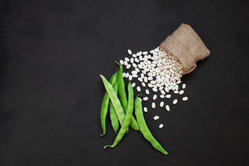 Uncooked dried white haricot beans in burlap sack with fresh raw green beans pod plant on rustic...