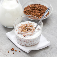 Breakfast buckwheat boiled with milk in a glass Cup on a light background