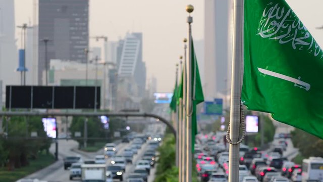 Saudi Arabia national flag waving and Riyadh's main street (King Fahd Road) on the background