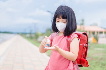 Asian kid girl student wearing face mask applying alcohol hand gel.Mini sanitizer pump.Reopen school from lockdown. Back to school.Covid-19 coronavirus pandemic.New normal lifestyle.Education concept