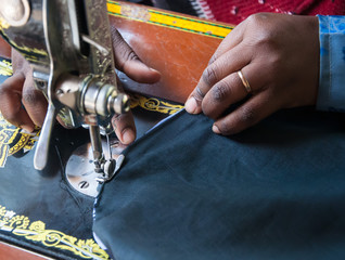 African woman seamstress with closeup of hands and a sewing machine, taken in a poverty region of...