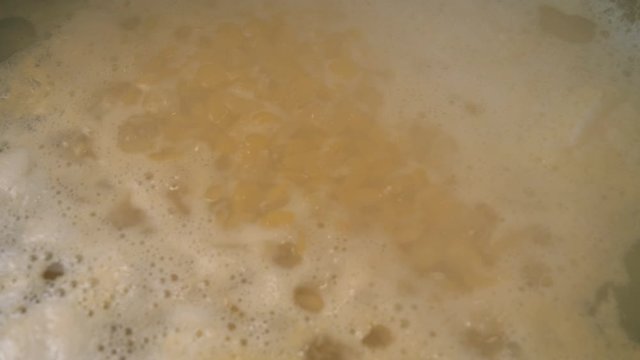 Preparing pea soup of split dry yellow peas in bubbling boiling water. Close up.