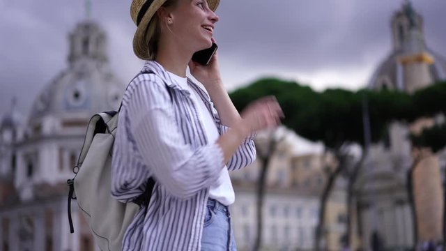 Slow motion of cheerful young woman blogger communicating with friend on smartphone using roaming connection. Hipster girl typing on screen text message during night walk in modern city
