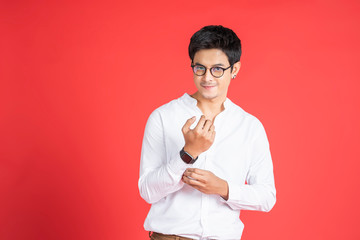 portrait handsome asian businessman adjusting his tshirt sleeve facial hair smiling looking straight wearing glasses and casual clothing and black earrings, standing and posing red isolated background