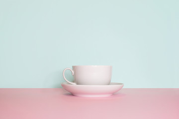 Side view on a still life. White cup with saucer on a bright pink and mint background. 