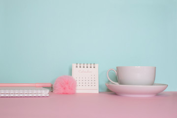 Side view on a still life. Pink fluffy pen, notepad and calendar on a pink table. Turquoise wall on the back