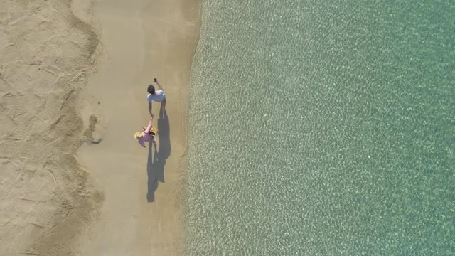 AERIAL DRONE TOP DOWN ZENITHAL CLOSE SHOT OF COUPLE WALKING HOLDING HANDS IN A PARADISE BEACH