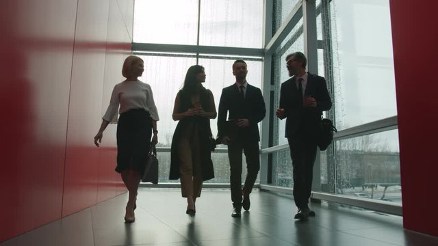 Dolly shot of well dressed businesspeople female and male walking in office center hall talking discussing business news. People, communication and lobby concept.