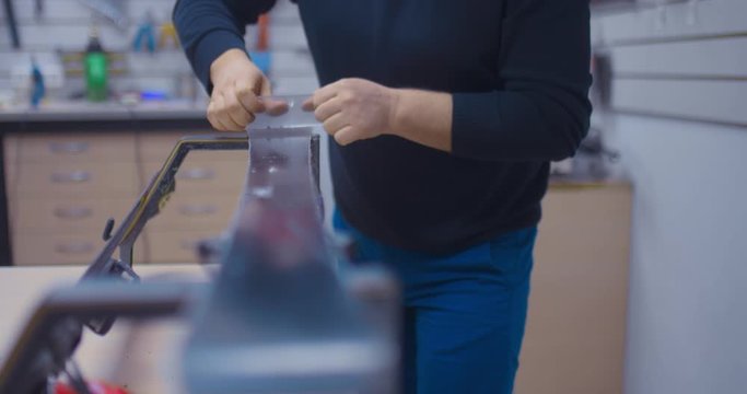 Professional repair of skis and snowboards, the workplace of the master. Hands scraper clean wax from skis, flying wax shavings. Close-up.