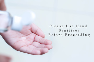 Close up a hand is using hand sanitizer from bottle for protective from gems on the hands with a reminder text " Please Use Hand Sanitizer Before Proceeding". Selective focus, simple and clean image.