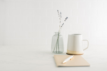 Fototapeta na wymiar Straight on view of clean, minimal desk with coffee mug, notebook and glass vase