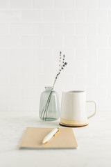 Straight on view of clean, minimal desk with coffee mug, notebook and glass vase