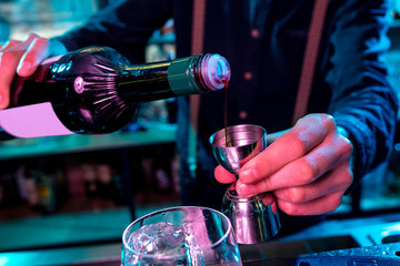 Close up of professional barman finishes preparation of alcoholic cocktail in multicolored neon light, gives it to client. Entertainment, drinks, service concept. Modern bar, trendy neoned colors.