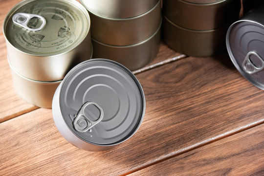 various tuna cans gold and silver color superimposed on each other with close view on brown wood