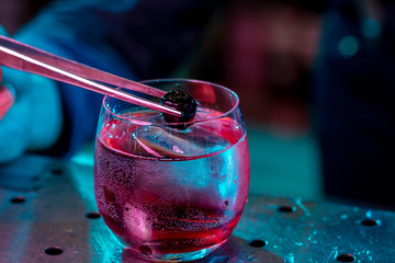 Close up of professional barman finishes preparation of alcoholic cocktail in multicolored neon...