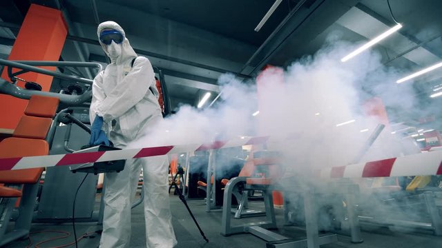 Specialist in a hazmat suit is fumigating the fitness center