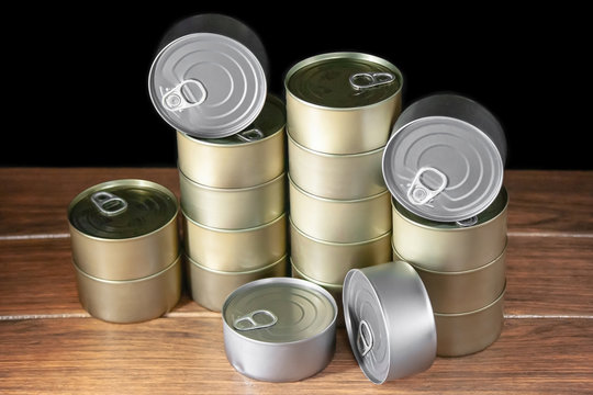 Many cans of tuna of gold and silver color placed by columns on brown wood and black background