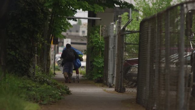 PORTLAND, OR - May 2020: Homeless man pushing a shopping cart away from the camera in slow motion