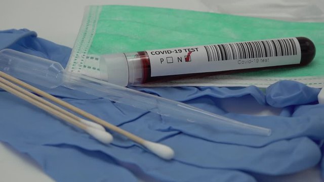 Close-up of test tube with negative result for Sars-Cov-2 coronavirus, rotating on table with rapid tes strip, a syringe needle, surgical gloves, cotton swabs, a medical mask and a pipette
