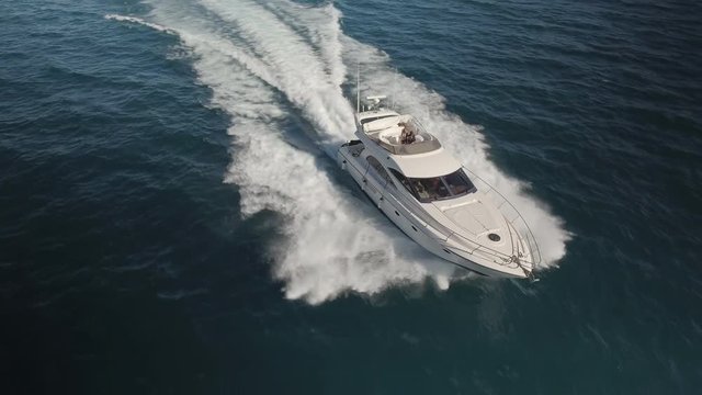 AERIAL DRONE FRONT SIDE VIEW AND ORBIT WITH FAST CHASE OF A LUXURY YACHT SAILING WITH GREAT SPEED IN BLUE DEEP SEA AND WHITE FOAM