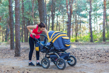 Fototapeta na wymiar Nature walk with stroller, young active mother in sportswear walking on the forest walkway with her baby in the pram, enjoying fresh air and smiling to the child
