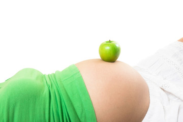 Pregnant woman laying down with a fresh green apple sitting on her baby pregnancy belly.