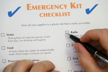 An emergency kit checklist is shown up close, just before being checkmarked by hand with an ink pen.