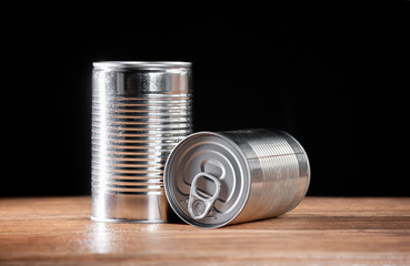 long cans of preserved products in silver color on brown wooden table and black background