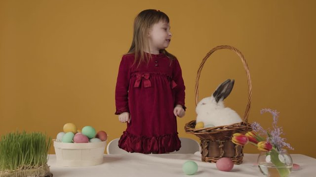 Happy little girl say wow. She is amazed. Little rabbit stay in basket, and table are full of easter eggs