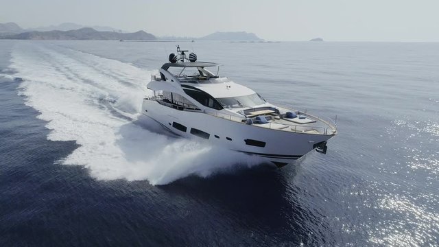 AERIAL DRONE FRONT SIDE VIEW FAST CHASE OF A LUXURY YACHT SAILING WITH GREAT SPEED IN BLUE DEEP SEA AND WHITE FOAM