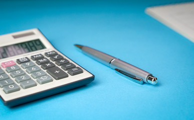 Calculator, pen and table calendar on blue background. Top view of office desk.