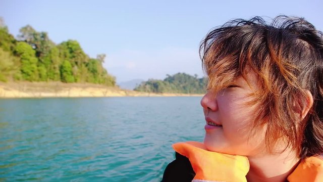 Slow motion , Happy young Asian woman wearing life jacket smiling relaxing refreshing with wind nature on longtail boat at “Cheow Lan Dam (Ratchaprapa Dam)”khao sok national park Suratthani Thailand.