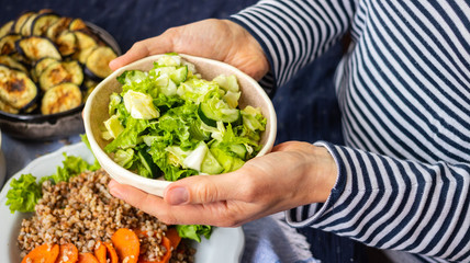 Woman hands hold vegetables on plate. Vegan healthy food. Lettuce, cucumbers salad