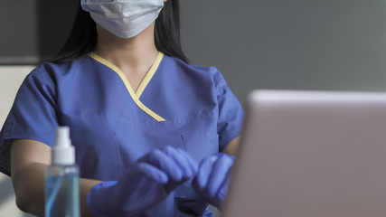 Female Medic in blue uniform works on computer sitting at table with sanitizer on it. Copy space at right side. Close up shot