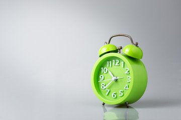 Green analog alarm clock gray background with light and shadow, copy space.