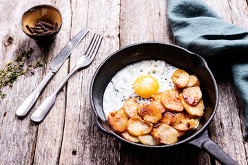 Fried Eggs and Potatoes in cast iron skillet on rustic wooden table. Skillet Breakfast. Selective focus