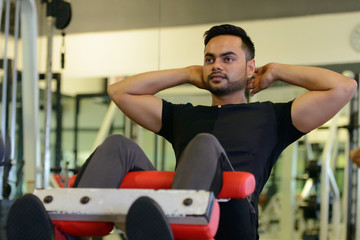 Obraz premium Full body shot of young bearded Indian man doing sit ups at the gym