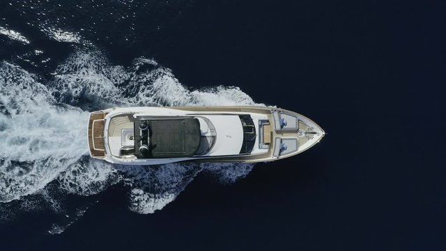 AERIAL DRONE STILL TOP-DOWN ZENITHAL VIEW OF LUXURY YACHT SAILING FROM SIDE TO SIDE IN BLUE DEEP SEA AND WHITE FOAM