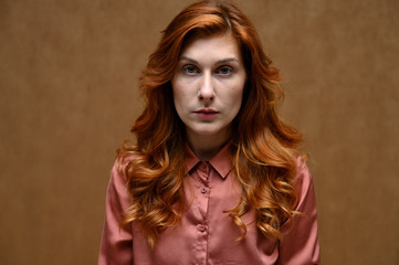 A pretty model is wearing a red shirt. Portrait of actress caucasian woman with red hair showing serious emotions. Photo taken in the studio on a beige background.