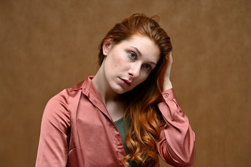 Photo portrait on a beige background of a caucasian calm pretty young woman in a pink shirt with long beautiful red hair. Studio shot.