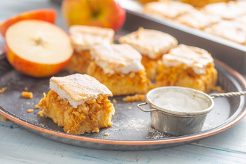Five cubes of apple plie with a cream topping, sugar sieve and half-cut apple next to it