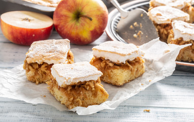 Three cubes of apple pie with a whisked wgg whites topping on a napkin with more pie and fresh apples in the back