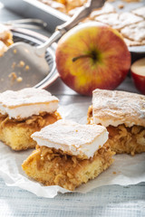 Portrait of three pieces of an apple pie with a whisked wgg whites topping on a napkin with more pie and fresh apples in the back