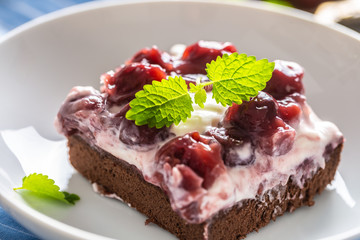 Detail of a piece of brownie with a cream, cherries and fresh mint leaves on a plate