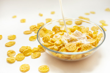 Side view of cornflakes to which milk is added in a transparent bowl on a white background