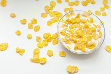 Corn flakes dipped in milk in a transparent bowl on a white background top view