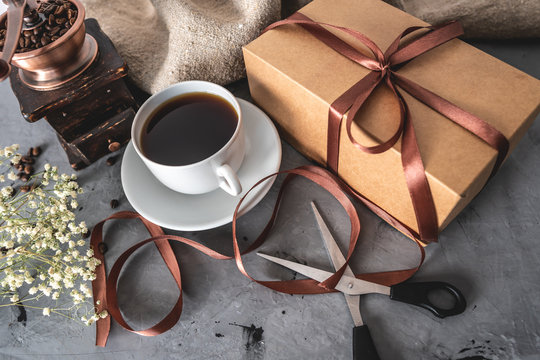Cup of freshly brewed black coffee, a gift box tied with brown ribbon, and a pair of scissors. Packaging a gift with your own hands during Breakfast or a break for a mug of aromatic drink
